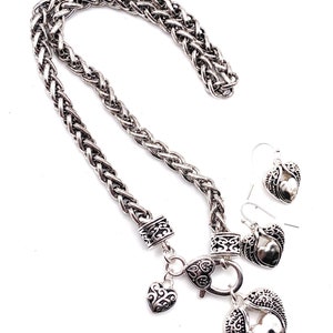 May include: Silver necklace with a braided chain and a heart pendant with wings. The necklace comes with matching earrings with heart pendants and wings.