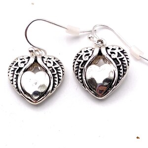 May include: A pair of silver dangle earrings with a heart-shaped design. The heart is surrounded by detailed wings.