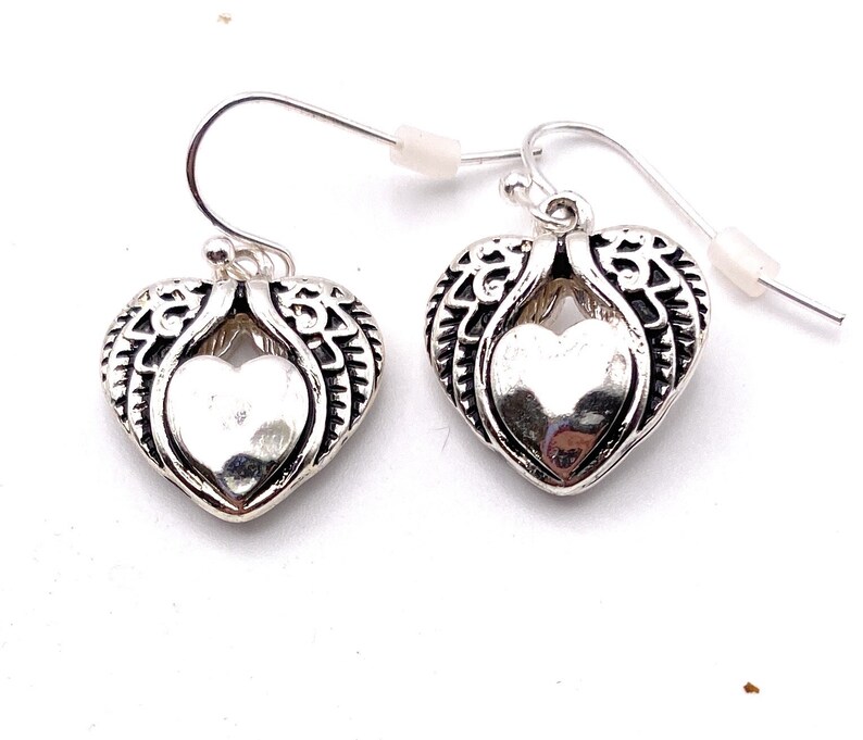 May include: A pair of silver dangle earrings with a heart-shaped design. The heart is surrounded by detailed wings.