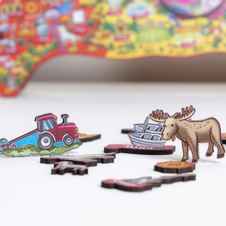 Op de afbeelding: Een houten puzzel met een rode tractor, een bruine eland en twee kleine boten. De puzzelstukken liggen op een wit oppervlak. De achtergrond is een wazig beeld van een kleurrijke kaart.
