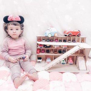 May include: A wooden toy car garage with a ramp and multiple levels for storing toy cars. A young child is playing with the garage and toy cars.