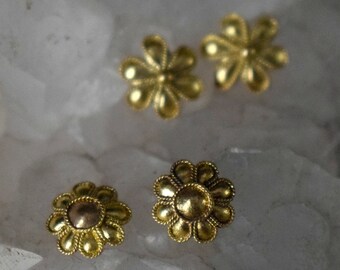 以下が含まれることがあります： 4つの金色の花の形をしたスタッドピアス。ピアスは、詳細な花びらのデザインと、中央にわずかに隆起した円形の要素を持っています。白い結晶質の表面に表示されています。