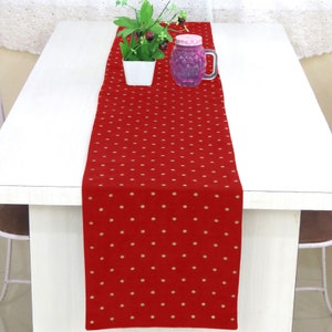 Peut inclure: Un chemin de table rouge à pois dorés. Le chemin de table est sur une table blanche avec une petite plante en pot et un bocal en verre.