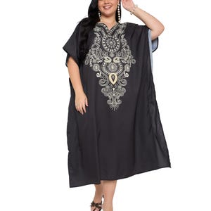 May include: A black kaftan dress featuring a V-neckline and intricate white embroidery patterns centered on the chest. The garment has loose, short sleeves and a flowing, knee-length silhouette made of a solid black fabric.