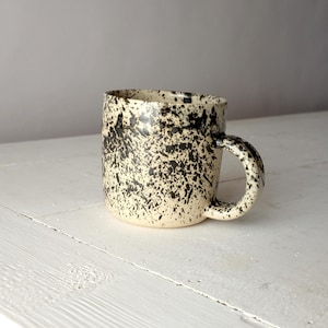 May include: A ceramic mug with a speckled black and white glaze. The mug has a rounded shape and a handle.