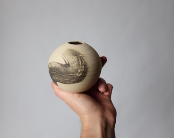 May include: A round ceramic vase with a black and white abstract design. The vase is being held in a hand.