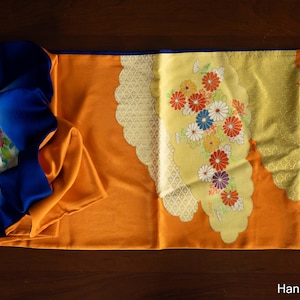 May include: An orange and blue textile with a floral design. The textile has a yellow section with a floral pattern in red, white, and purple. The text "Hanami Clothing" is visible at the bottom.