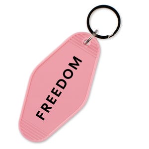 May include: A pink motel-style keychain with the word "FREEDOM" printed in black. The keychain has a ridged design at the top and bottom and a black metal keyring.