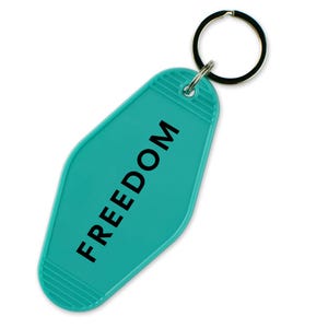May include: Teal-colored motel-style keychain with the word "FREEDOM" printed in black. The keychain has a rounded rectangular shape with a ridged design at the bottom and a metal ring for attaching keys.