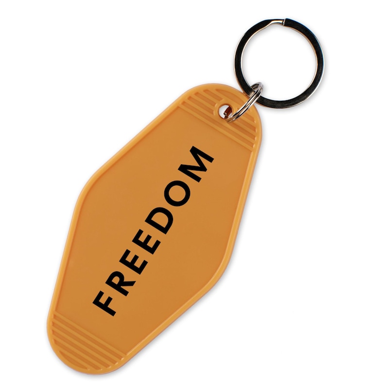 May include: An orange motel-style keychain with the word "FREEDOM" printed in black. The keychain has a metal ring attached for keys. The background is white.