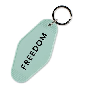 May include: A light teal motel-style keychain with the word "FREEDOM" printed in black. The keychain has a metal ring attached for keys. The background is white.