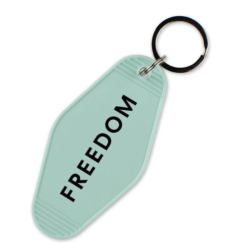 May include: A light teal motel-style keychain with the word "FREEDOM" printed in black. The keychain has a metal ring attached for keys. The background is white.