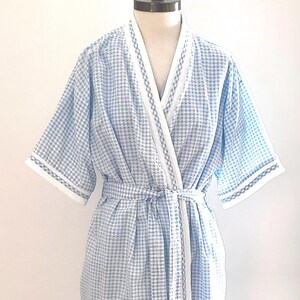 May include: A light blue and white gingham patterned robe with a white trim. The robe has short sleeves and a matching belt. The robe is displayed on a mannequin.