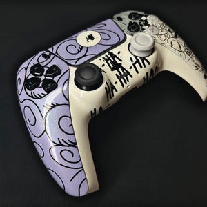 May include: A wireless video game controller featuring a custom design with a light purple base covered in black swirl patterns. The center and right side are cream-colored with black text reading HA-HA-HA and a small black graphic of a figure.