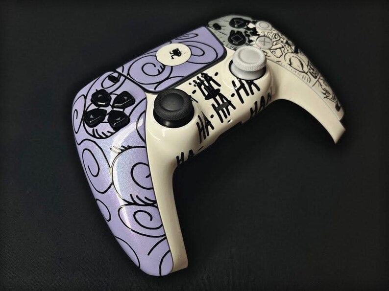May include: A wireless video game controller featuring a custom design with a light purple base covered in black swirl patterns. The center and right side are cream-colored with black text reading HA-HA-HA and a small black graphic of a figure.