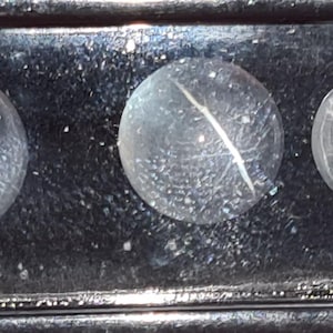 May include: Five clear, spherical star quartz gemstones with a star-like pattern. The gemstones are displayed on a dark surface. A small white label reads "Star quartz 5 pcs 39 cts".