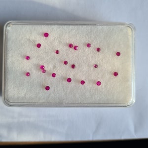 Könnte beinhalten: Eine weiße Schale mit 18 kleinen, runden, rosafarbenen Edelsteinen, die in einem Muster angeordnet sind.