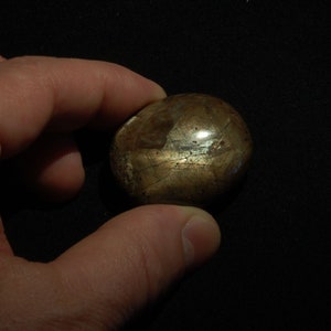 Könnte beinhalten: Ein runder, goldbrauner Edelstein mit einer glatten, polierten Oberfläche. Der Stein hat einen dezenten Schimmer und einige sichtbare Einschlüsse.