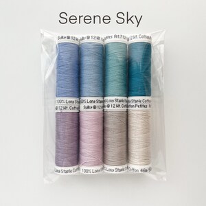 May include: A set of six spools of thread in shades of blue, purple, pink, gray, and white. The thread is labeled "Sulky 12 Wt. Cotton" and "Long Staple Cotton".