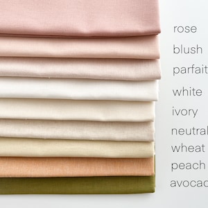 May include: A stack of ten fabric swatches in various shades of pink, white, beige, brown, and green. The swatches are labeled with the following colors: rose, blush, parfait, white, ivory, neutral, wheat, peach, and avocado.