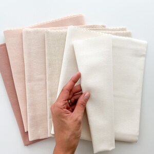 May include: A stack of six fabric swatches in various shades of pink and white. The swatches are folded and arranged in a gradient from darkest pink to white.