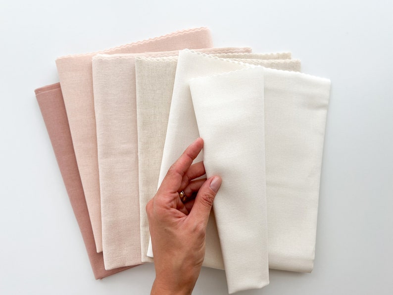 May include: A stack of six fabric swatches in various shades of pink and white. The swatches are folded and arranged in a gradient from darkest pink to white.