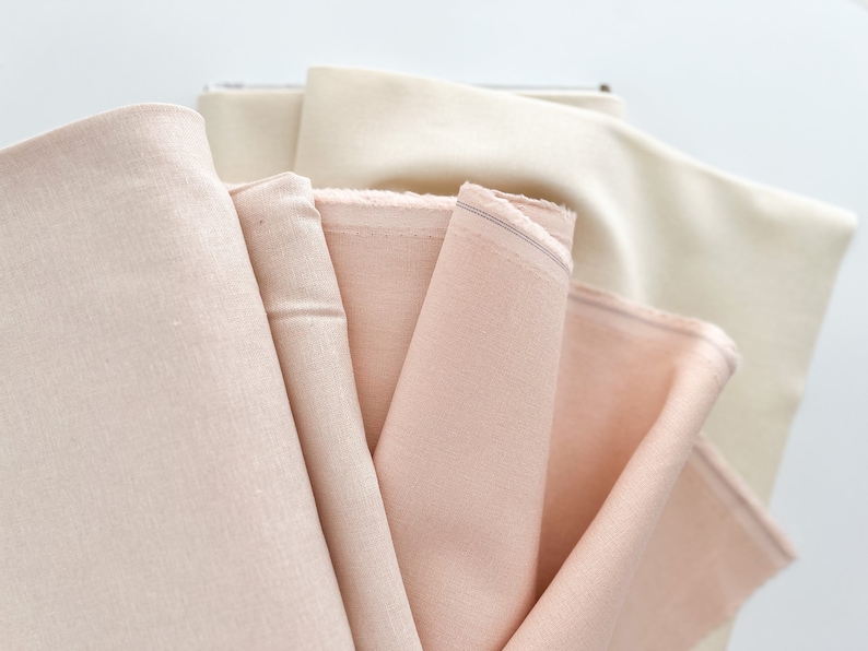 May include: A stack of four fabric swatches in various shades of pink and cream. The fabric is smooth and has a subtle sheen.