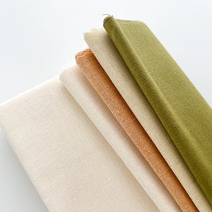 May include: A stack of five fabric swatches in different colors and textures. The top swatch is a dark green, the next is a light green, followed by a beige, then a light orange, and finally a white swatch.