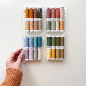 May include: Assortment of 20 spools of 100% cotton thread in various colors, including shades of brown, green, blue, and yellow. Each spool is labeled with the brand name "Sulky" and the thread weight "12wt".