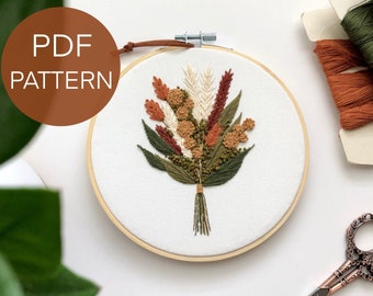 May include: Embroidered hoop art featuring a floral bouquet in shades of green, brown, and white. The hoop is made of wood and has a white fabric background. The text "PDF PATTERN" is visible in the top left corner of the image.