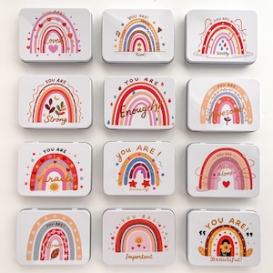May include: A collection of twelve white rectangular tins, each adorned with a colorful rainbow design and uplifting text. The text includes words like "Loved," "Kind," "Worthy," "Strong," and "Enough." The tins are arranged in a grid pattern.