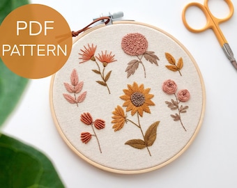 May include: Embroidered hoop art featuring a variety of floral designs in shades of orange, yellow, and pink. The hoop is made of wood and has a white fabric background. The text "PDF PATTERN" is visible in the top left corner of the image.