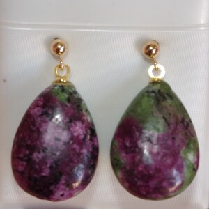 Könnte beinhalten: Ein Paar tropfenförmige Ohrringe mit grünen und violetten Edelsteinen und goldfarbenen Metallakzenten.