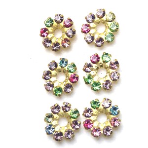 Pode incluir: Seis enfeites de metal dourado em forma de flor com um furo central. Cada flor tem um anel de strass coloridos.