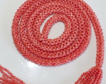 May include: A strand of coral beads in a bright pink colour. The beads are small and round, and the strand is long enough to be worn as a necklace.