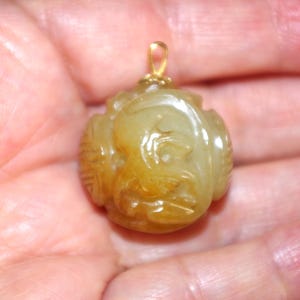 May include: A round, yellow-green jade pendant with intricate carvings. The pendant has a gold bail and is suspended from a chain.