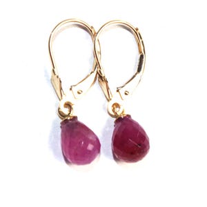 May include: A pair of gold earrings with pink gemstone drops. The earrings have a lever back closure.
