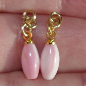May include: A pair of pink shell earrings with gold-toned metal clasps. The earrings are oval shaped and have a smooth, polished finish.
