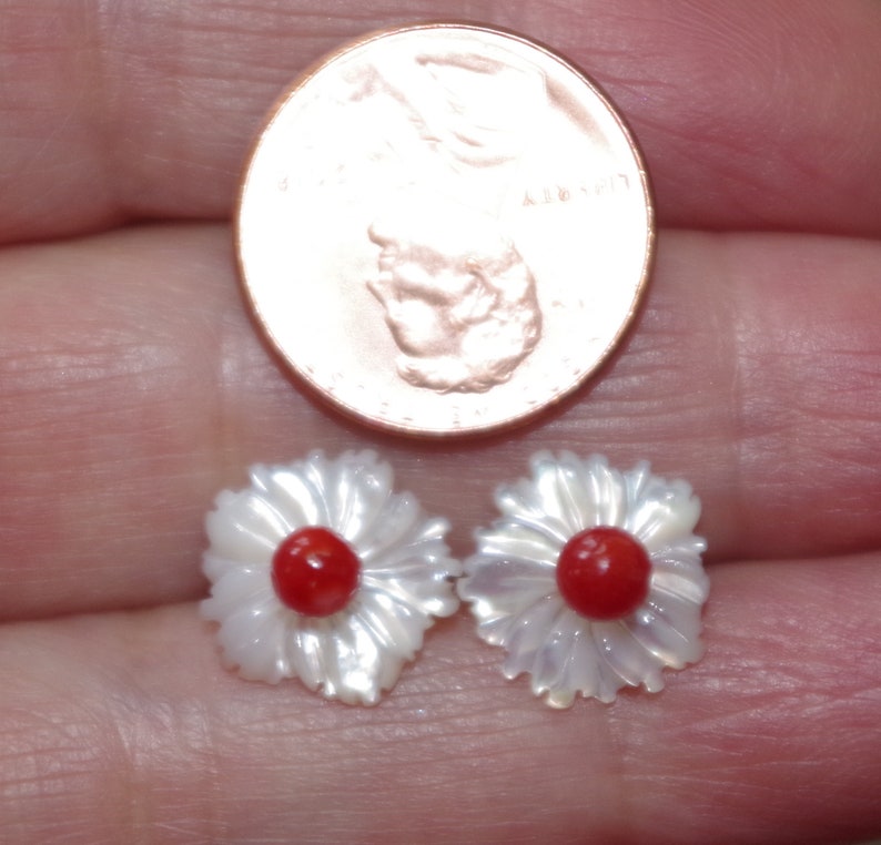 May include: A pair of daisy-shaped stud earrings. The earrings have white, iridescent petals and a bright red center. A penny is next to the earrings for size comparison.