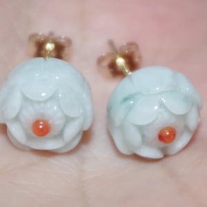 Könnte beinhalten: Ein Paar Jade-Blumenohrringe mit roter Mitte. Die Ohrringe sind aus weißem Jade und haben eine goldene Rückseite.