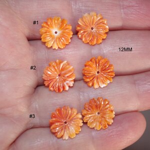 Puede incluir: Tres cuentas de flores de concha talladas en naranja y blanco, cada una con un agujero en el centro. Las cuentas tienen 12 mm de diámetro. #1, #2 y #3 están escritos junto a cada cuenta.
