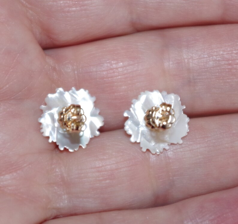 May include: A pair of flower-shaped stud earrings. Each earring features a white, petal-like design surrounding a gold-colored center. The earrings are small and delicate, suitable for everyday wear.