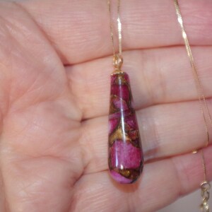 May include: A gold chain necklace with a teardrop-shaped pendant. The pendant is made of a pink and gold material with a marbled pattern.