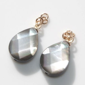 May include: Two pearlescent teardrop-shaped beads with gold-toned metal loops at the top. The beads have a faceted, iridescent finish.