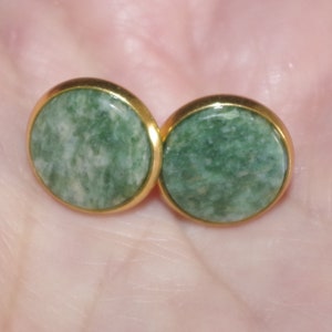 May include: A pair of gold stud earrings with green stone insets. The stones have a mottled green and white pattern.