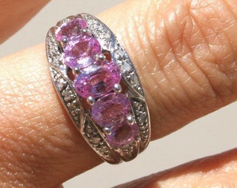 May include: A silver ring with a row of five pink oval gemstones set in a decorative band with smaller diamonds.