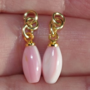 May include: A pair of pink shell earrings with gold-toned metal clasps. The earrings are oval shaped and have a smooth, polished finish.