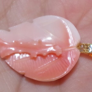 May include: A pink and white shell pendant with a gold chain and clear gemstones. The shell is carved into a leaf shape.