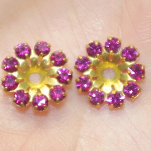 May include: Two gold-toned flower-shaped embellishments with a central hole. Each embellishment has ten pink rhinestones.
