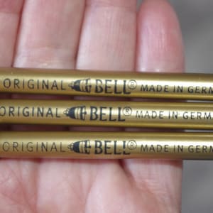 Puede incluir: Tres minas de lápiz mecánico de color dorado con letras negras que dicen "ORIGINAL BELL® MADE IN GERMANY".